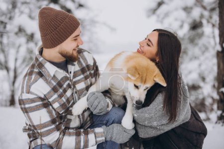 Foto de Feliz pareja joven con un perro akita en el bosque en invierno y día nevado - Imagen libre de derechos