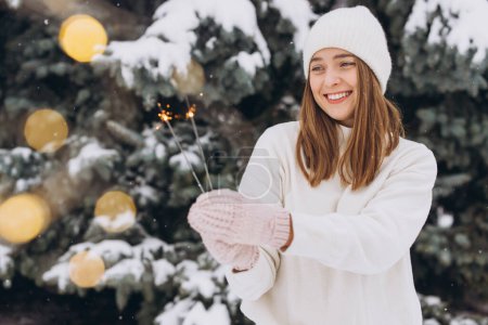 Foto de Retrato de niña sonriente con sombrero de punto blanco, bufanda, manoplas y suéter con bengala en invierno al aire libre. Vacaciones de Navidad - Imagen libre de derechos