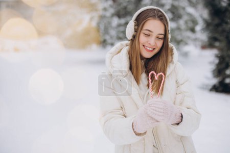 Foto de Una linda chica en mitones de punto sostiene bastones de caramelo en forma de corazón en el parque de invierno - Imagen libre de derechos