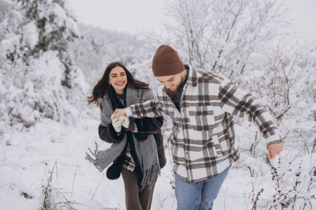 Téléchargez les photos : Un jeune couple heureux et aimant se promène dans une forêt enneigée dans les montagnes - en image libre de droit