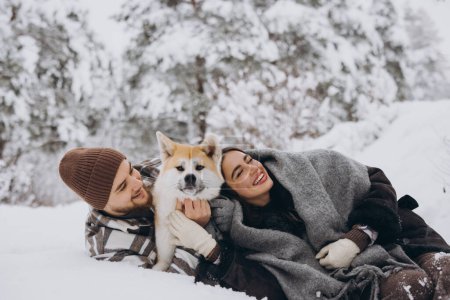 Téléchargez les photos : Joyeux jeune couple avec chien akita en forêt le jour de l'hiver - en image libre de droit