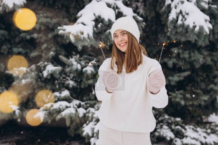 Téléchargez les photos : Portrait de fille souriante portant un chapeau en tricot blanc, une écharpe, des mitaines et un pull avec un éclat en hiver à l'extérieur. Vacances de Noël - en image libre de droit
