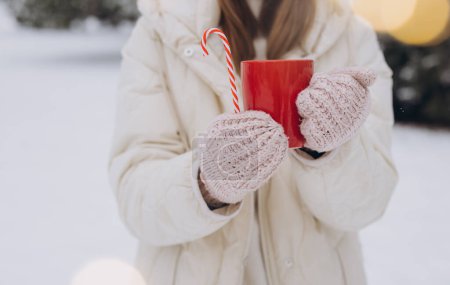 Foto de Linda mujer feliz en manoplas de punto con café caliente con bastones de caramelo en el parque de invierno - Imagen libre de derechos
