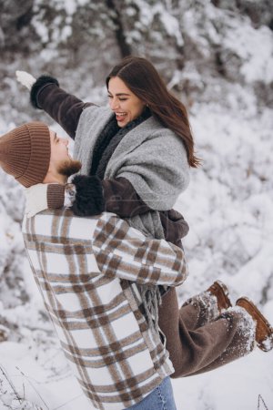 Téléchargez les photos : Un jeune couple heureux et aimant se promène dans une forêt enneigée hivernale en montagne - en image libre de droit