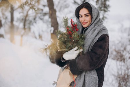Photo for Happy pretty smiling woman holding bouquet of pine tree in snowy forest in winter. - Royalty Free Image