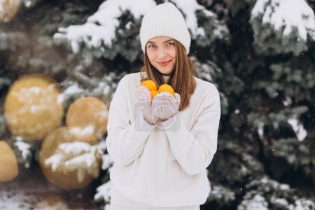 Téléchargez les photos : Une belle fille heureuse en tricot blanc tient des mandarines en hiver sur un fond de pin - en image libre de droit