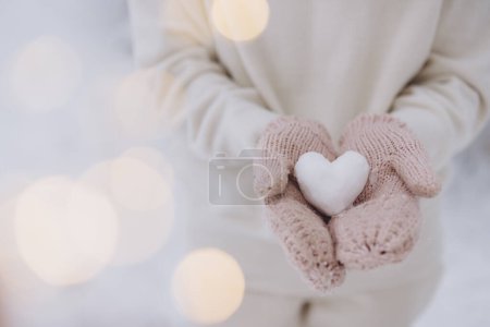 Photo for Female hands in knitted mittens hold a snow heart on a winter background - Royalty Free Image