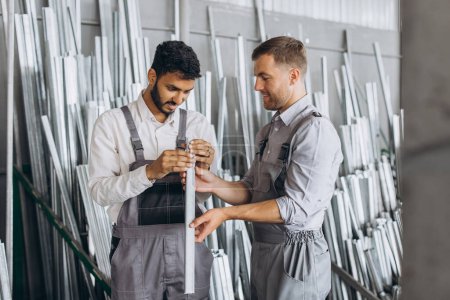 Foto de Dos trabajadores masculinos internacionales en uniforme discuten el proceso de trabajo en una fábrica de ventanas de metal y plástico - Imagen libre de derechos