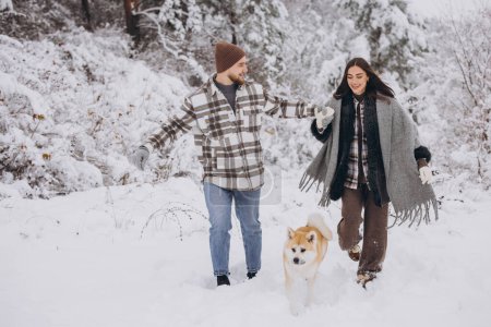 Foto de Feliz pareja joven con un perro akita en el bosque en invierno y día nevado - Imagen libre de derechos