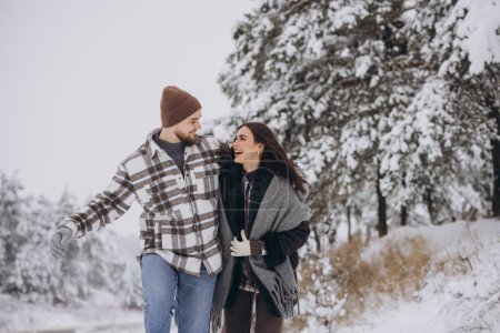 Téléchargez les photos : Un jeune couple heureux et aimant se promène dans une forêt enneigée hivernale en montagne - en image libre de droit