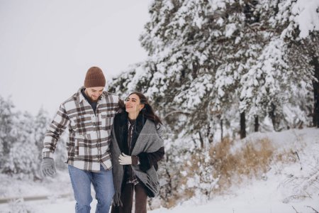 Photo for A young happy and loving couple walking in a winter snowy forest in the mountains - Royalty Free Image