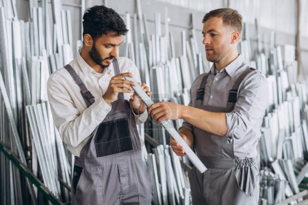 Téléchargez les photos : Deux travailleurs masculins internationaux en uniforme discutent du processus de travail dans une usine de fenêtres métal-plastique - en image libre de droit