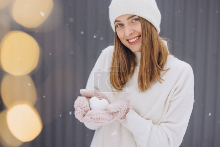 Téléchargez les photos : Femme heureuse en mitaines tricotées tenant un cœur de neige par une journée enneigée d'hiver - en image libre de droit