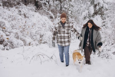 Téléchargez les photos : Joyeux jeune couple avec chien akita en forêt en hiver et journée enneigée - en image libre de droit