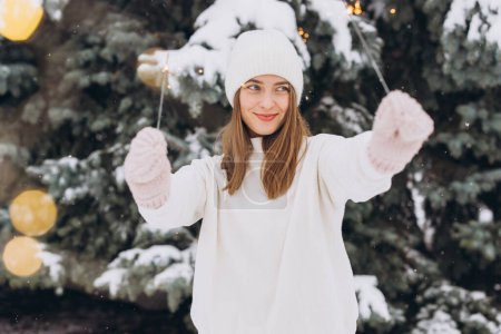 Foto de Retrato de niña sonriente con sombrero de punto blanco, bufanda, manoplas y suéter con bengala en invierno al aire libre. Vacaciones de Navidad - Imagen libre de derechos