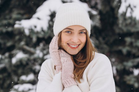 Foto de Retrato de una hermosa chica feliz en ropa blanca de punto posando en un abrigo de invierno en un día nevado - Imagen libre de derechos