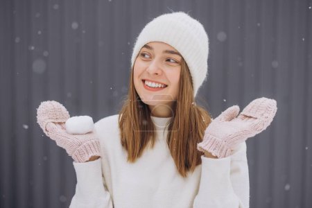Téléchargez les photos : Joyeux jeune femme en moufles tricotées attrape flocons de neige en hiver - en image libre de droit
