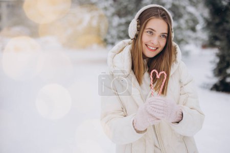 Foto de Una linda chica en mitones de punto sostiene bastones de caramelo en forma de corazón en el parque de invierno - Imagen libre de derechos