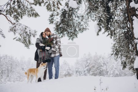 Foto de Feliz pareja joven con un perro akita en el bosque en el día de invierno - Imagen libre de derechos