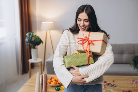 Téléchargez les photos : Belle femme heureuse emballe et tient des cadeaux de Noël à la maison - en image libre de droit