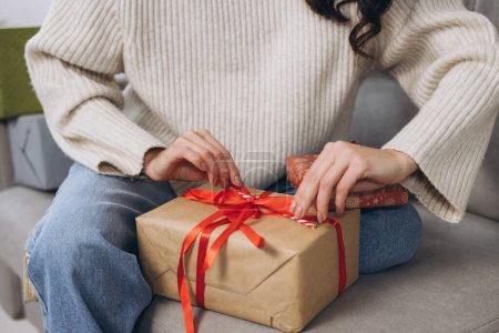 Téléchargez les photos : Les mains féminines déballer des cadeaux de Nouvel An ou de Noël à la maison sur le canapé - en image libre de droit