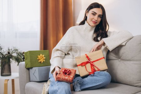 Foto de Hermosa mujer feliz desenvolviendo regalos de Año Nuevo o Navidad en casa en el sofá - Imagen libre de derechos