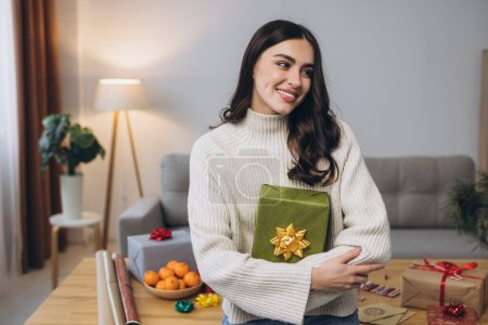 Téléchargez les photos : Belle femme heureuse emballe et tient des cadeaux de Noël à la maison - en image libre de droit