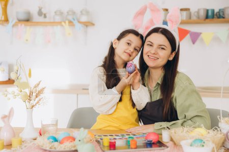Photo for Mother and her daughter painting eggs. Happy family preparing for Easter. Cute little child girl wearing bunny ears. - Royalty Free Image