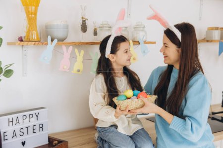 Foto de Madre y su hija sosteniendo canasta de huevos de colores. Familia feliz preparándose para la Pascua. Linda niña pequeña con orejas de conejito. - Imagen libre de derechos