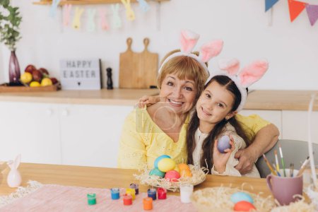 Téléchargez les photos : Joyeux Pâques ! Une grand-mère et sa petite-fille peignent des œufs de Pâques. Bonne famille se préparant pour Pâques. Petite fille mignonne portant des oreilles de lapin le jour de Pâques
. - en image libre de droit