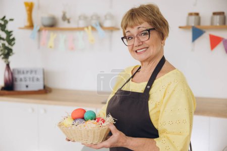 Téléchargez les photos : Joyeux Pâques ! Mignon retraité vieille femme peint oeufs de Pâques sur la cuisine à la maison. Oeufs de Pâques bricolage - en image libre de droit