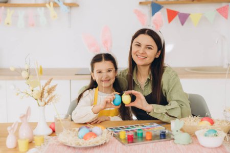 Photo for Mother and her daughter hugging each other and holding colorful eggs. Happy family preparing for Easter. Cute little child girl wearing bunny ears. - Royalty Free Image