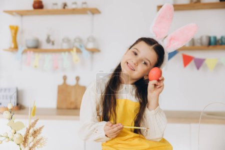 Foto de ¡Feliz Pascua! Linda niña sosteniendo coloridos huevos de Pascua y divertirse en la cocina en casa. Niña con orejas de conejo el día de Pascua. - Imagen libre de derechos