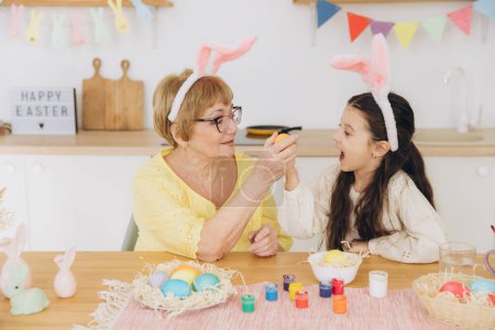 Photo for Happy grandmother and granddaughter in easter bunny ears having egg tapping with easter eggs at modern home in sunny spring day - Royalty Free Image