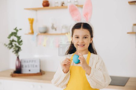 Téléchargez les photos : Joyeux Pâques ! Une belle fille enfant peignant des œufs colorés et amusez-vous. Mignon enfant fille portant des oreilles de lapin le jour de Pâques. - en image libre de droit