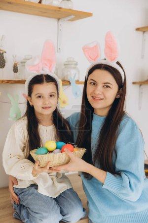 Téléchargez les photos : Mère et sa fille tenant un panier d'œufs colorés. Bonne famille se préparant pour Pâques. Petite fille mignonne portant des oreilles de lapin. - en image libre de droit