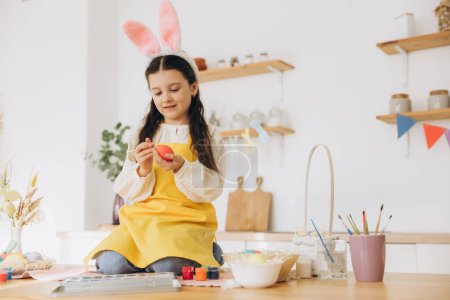 Photo for Happy easter! A beautiful child girl sitting on the table with decoratioons and painting colorful eggs. Cute child girl wearing bunny ears on Easter day. - Royalty Free Image