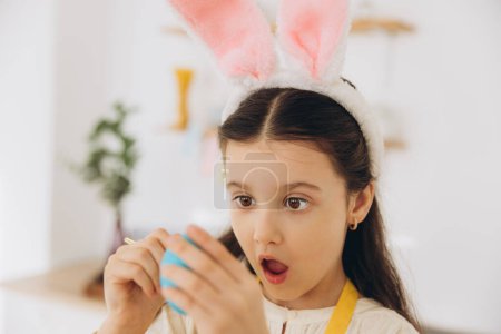 Foto de ¡Feliz Pascua! Una hermosa niña pintando huevos de colores y divertirse. Linda niña con orejas de conejo en el día de Pascua. - Imagen libre de derechos