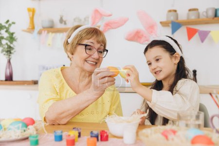 Photo for Happy grandmother and granddaughter in easter bunny ears having egg tapping with easter eggs at modern home in sunny spring day - Royalty Free Image