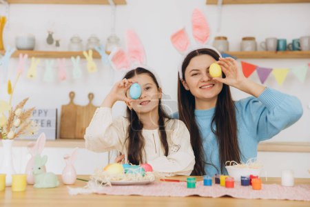 Téléchargez les photos : Mère et sa fille tenant des œufs colorés. Bonne famille se préparant pour Pâques. Petite fille mignonne portant des oreilles de lapin. - en image libre de droit