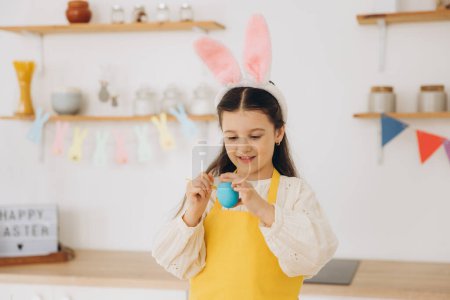 Foto de ¡Feliz Pascua! Una hermosa niña pintando huevos de colores y divertirse. Linda niña con orejas de conejo en el día de Pascua. - Imagen libre de derechos