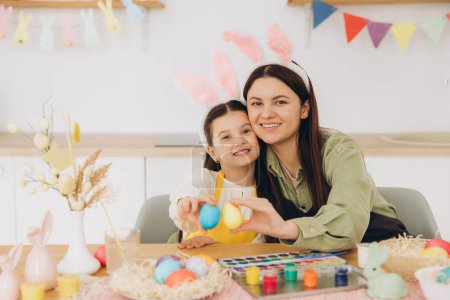 Photo for Mother and her daughter hugging each other and holding colorful eggs. Happy family preparing for Easter. Cute little child girl wearing bunny ears. - Royalty Free Image