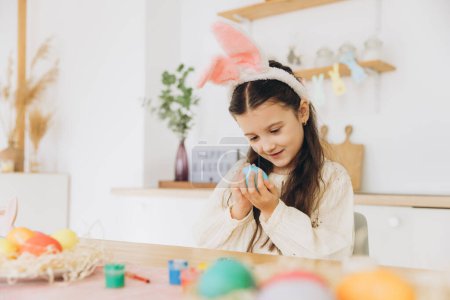 Téléchargez les photos : Joyeux Pâques ! Une belle enfant fille peignant des œufs de Pâques. Petite fille mignonne portant des oreilles de lapin le jour de Pâques. - en image libre de droit