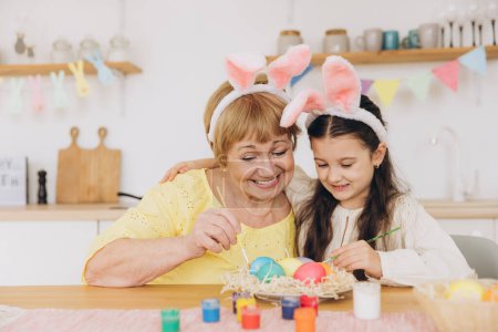 Téléchargez les photos : Joyeux Pâques ! Une grand-mère et sa petite-fille peignent des œufs de Pâques. Bonne famille se préparant pour Pâques. Petite fille mignonne portant des oreilles de lapin le jour de Pâques
. - en image libre de droit