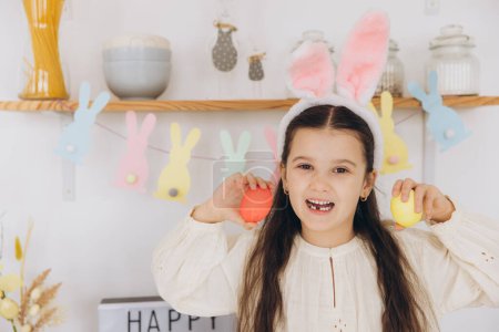 Téléchargez les photos : Joyeux Pâques ! Une belle fille enfant peignant des œufs colorés et amusez-vous. Mignon enfant fille portant des oreilles de lapin le jour de Pâques. - en image libre de droit