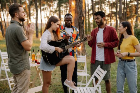 Foto de Atractiva mujer hipster tocando la guitarra ganando a los hombres en la cena con amigos multirraciales - Imagen libre de derechos