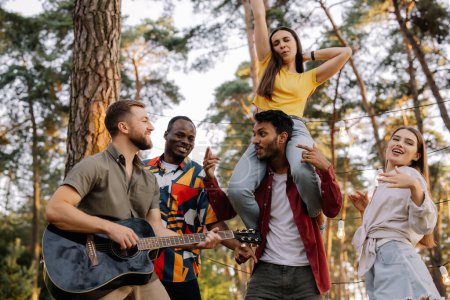 Photo for Multiracial group of people, bearded hipster man playing guitar and friends dancing, singing and having fun - Royalty Free Image