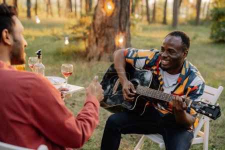 Photo for African man plays the guitar for Indian man who drinks wine and sings - Royalty Free Image