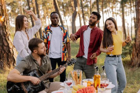 Photo for Multicultural group of people, bearded hipster man playing guitar and friends dancing and having fun - Royalty Free Image