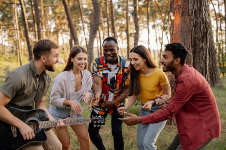 Foto de Grupo multirracial de personas, hipster barbudo tocando la guitarra y amigos bailando, cantando y divirtiéndose - Imagen libre de derechos